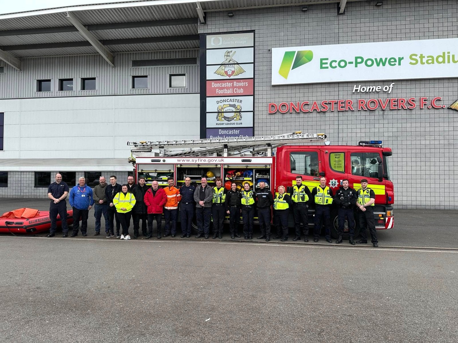 A group beside a fire engine and a water-rescue boat outside Doncaster Rovers' Eco-Power Stadium.