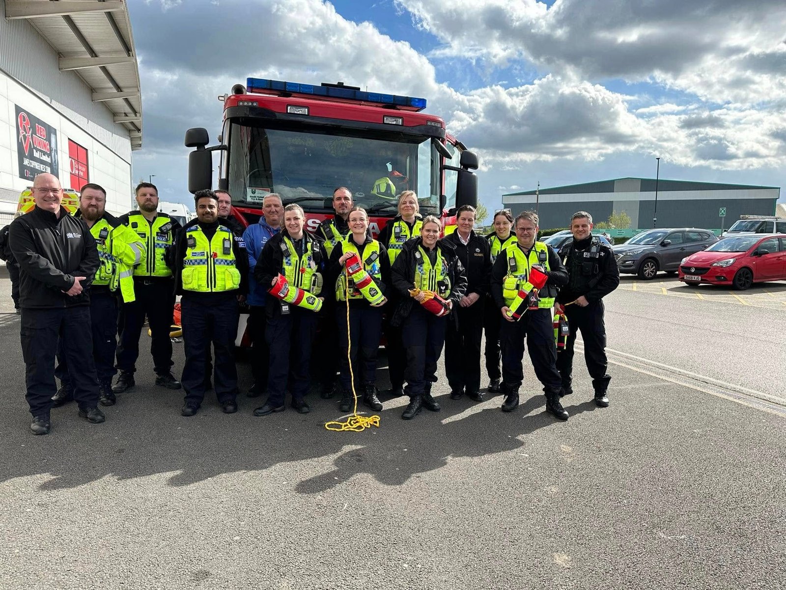 A group in hi-vis jackets holding orange throwlines in front of a fire engine.